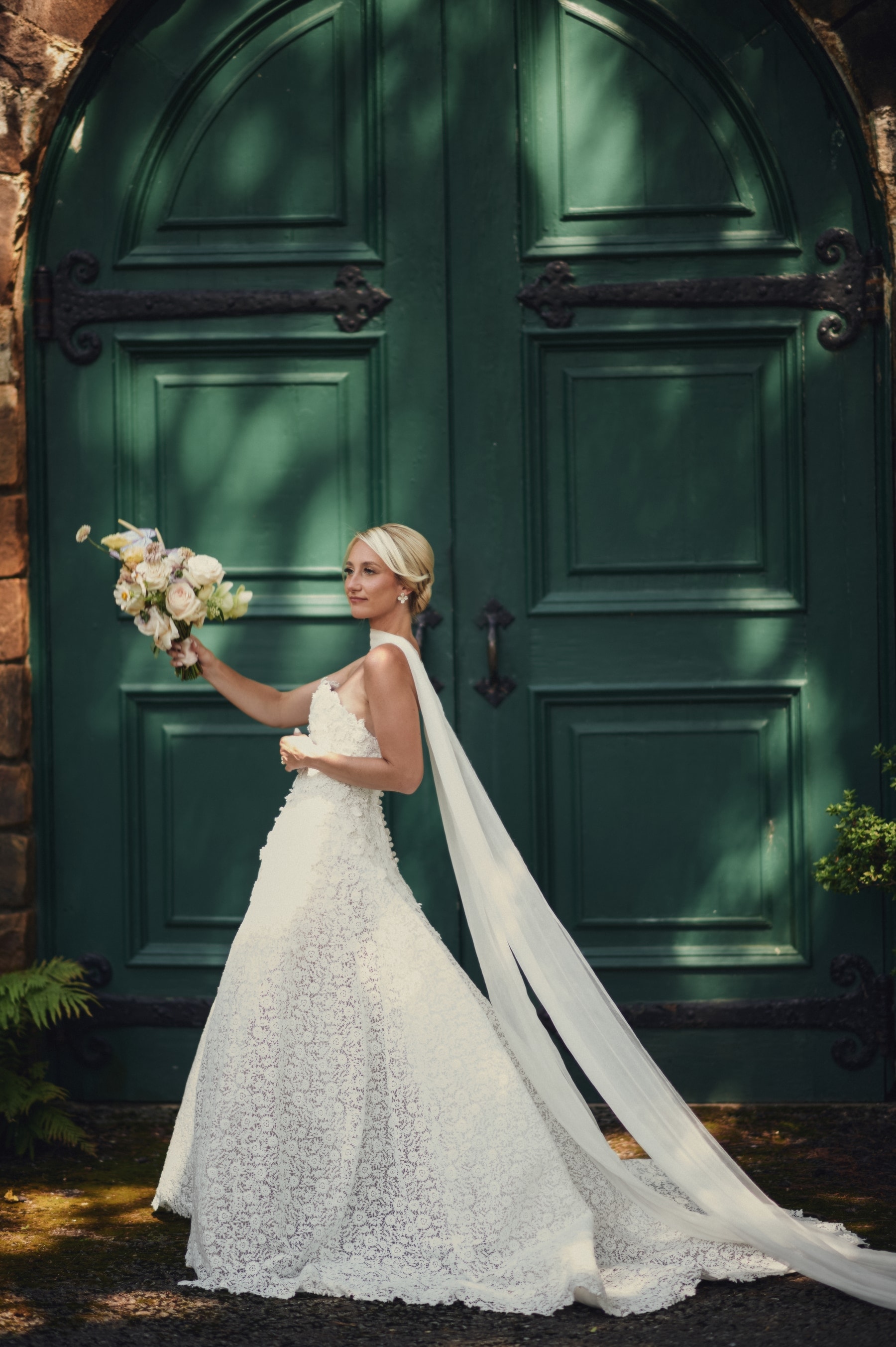 Christine with her bouquet before the deep-green doors of Strong Mansion, veil to the ground